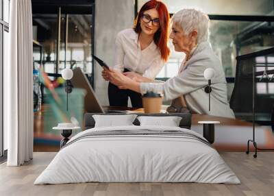 Old female manager looking at tablet with paperwork with employee. Wall mural