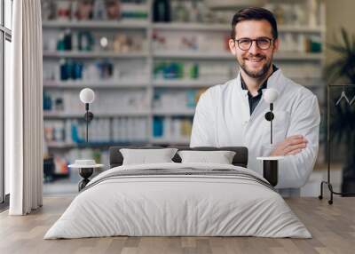 Picture of a young happy pharmacist standing with arms crossed and smiling at the camera. Wall mural