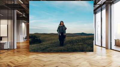 Portrait of a stylish woman hiking on a mountain path with tall grass Wall mural