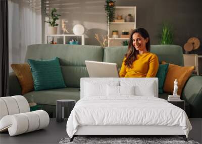 Portrait of a woman using laptop while sitting on a mint couch at home Wall mural