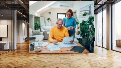 Senior couple sitting at table and looking into blueprints of their new home Wall mural