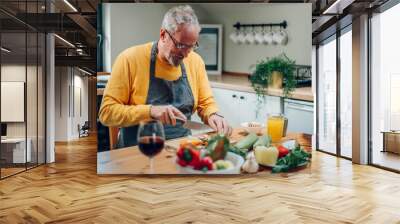 Senior man in apron preparing food at the kitchen counter and cooking a meal Wall mural