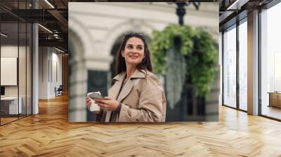 Smiling businesswoman walking in the city and using smartphone Wall mural