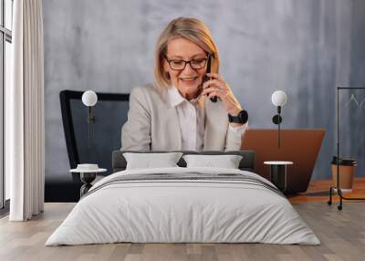 Smiling mature businesswoman talking on phone and writing in agenda. Wall mural