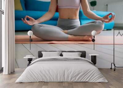 woman siting in a lotus yoga position on the fitness mat at home Wall mural