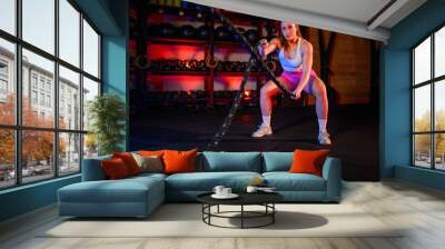 Woman training in a fitness gym while exercising with a battle ropes Wall mural