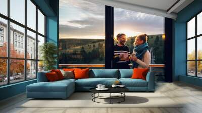 Young couple drinking coffee or tea while standing on their balcony at sunrise Wall mural