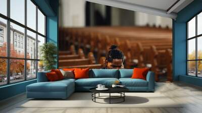 Young man praying in church pew holding rosary beads Wall mural