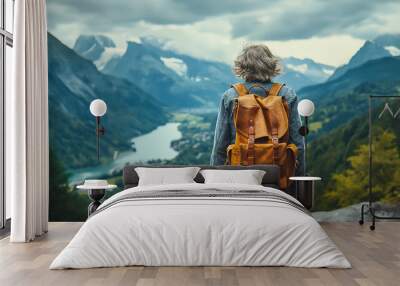 A traveler stands at a mountain overlook, gazing at breathtaking peaks and a serene lake nestled below. The lush landscape showcases nature’s beauty on a perfect vacation day Wall mural