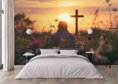 back view of man sitting on the flowers meadow and looking on cross. Easter tranquil scene Wall mural