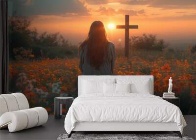 back view of woman sitting on the flowers meadow and looking on cross. Easter tranquil scene Wall mural