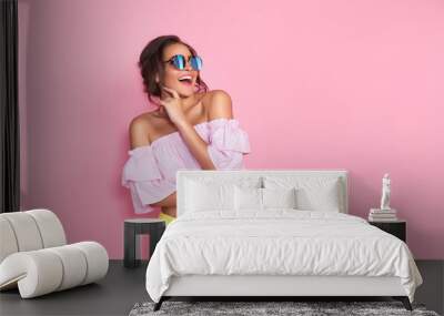 Beautiful girl in colorful clothes wearing sunglasses posing on pink background in studio. Wall mural