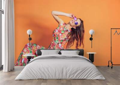 Girl in floral dress emotionally poses on the orange background. Wall mural