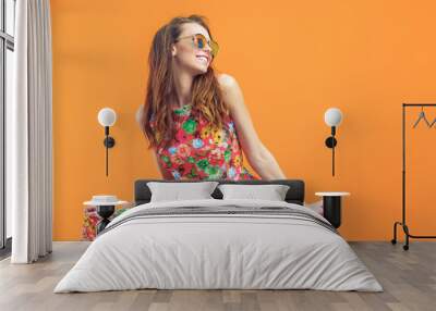 Girl in floral dress emotionally poses on the orange background. Wall mural