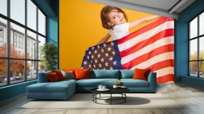 Happy child, cute girl with American flag on yellow studio background. USA celebrate July 4th, independence Day. Wall mural