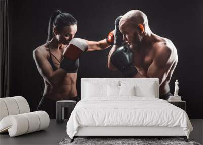 Shirtless Woman exercising with trainer at boxing and self defense lesson, studio, dark background. Female and male fight. Wall mural