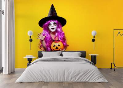 Small girl in Halloween witch dress and hat scaring and making faces isolated on yellow background. Trick or treat. Wall mural