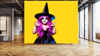 Small girl in Halloween witch dress and hat scaring and making faces isolated on yellow background. Wall mural