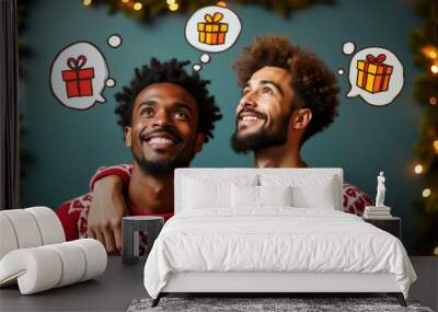 Two men, an interracial couple, gaze upwards with joyful expressions, envisioning gifts in thought bubbles. They are dressed in matching holiday sweaters, embodying festive spirit Wall mural