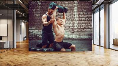 Two muscular athletes training, one raise, push the barbbell when other is motivating. Scream. Working hard. Street gym. Exercise for the shoulder muscles, deltoid. Wall mural