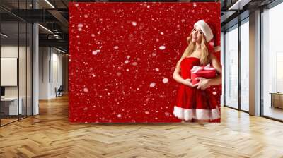 Woman wearing stylish red dress of Christmas costume posing with gift box in snow Wall mural