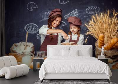 Woman with little girl in hats and aprons making pastries from dough and having fun together being messy in flour Wall mural