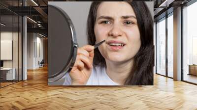 A woman in front of a mirror plucking hairs above her upper lip. Removing the mustache with tweezers yourself. Wall mural