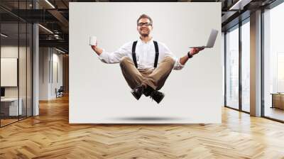 Young man is soaring in the air with a Cup of coffee and a laptop Wall mural