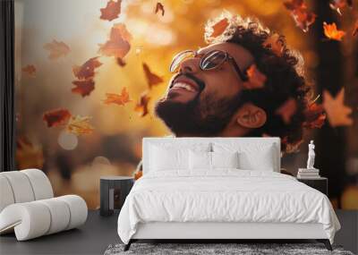 smiling ethnic man guy with eyes closed in the park outdoors in autumn surrounded by falling leaves floating in the air movement motion wearing hat curly hair glasses beard Wall mural