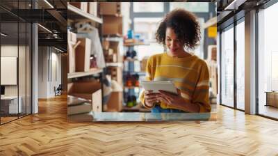 A young woman in her home office is sitting at the table, surrounded by boxes of products on which she has just been working with an iPad. She looks happy while opening up Wall mural