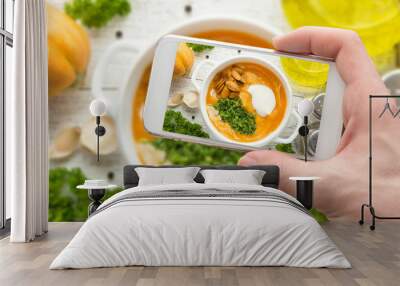 Man's hand takes photo of hot pumpkin soup with seasoning with smart phone Wall mural