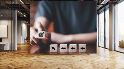 Businessman holding wooden cube with target board icon and arrow on wooden table. Goals and planning for success in marketing business, achieve the objective concept. Closeup and free copy spac Wall mural