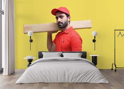 delivery man in red t shirt and cap holding packing box yellow background  indian pakistani model Wall mural