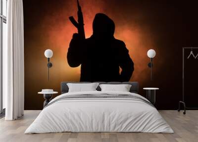 Silhouette of man with assault rifle ready to attack on dark toned foggy background or dangerous bandit in black wearing balaclava and holding gun in hand. Shooting terrorist with weapon theme decor Wall mural