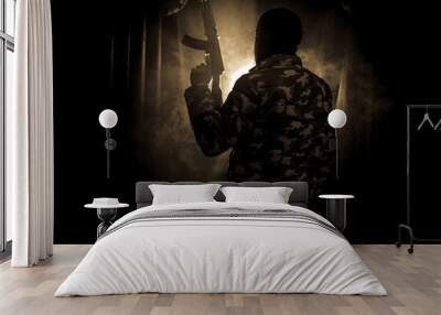 Silhouette of man with assault rifle ready to attack on dark toned foggy background or dangerous bandit in black wearing balaclava and holding gun in hand. Wall mural