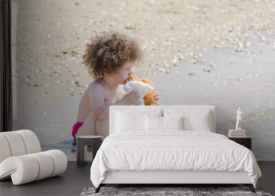 beautiful curly hair child eating donut on beach Wall mural