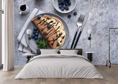 Crepe with banana, chocolate sauce and blueberries for breakfast on a stone background. Wall mural