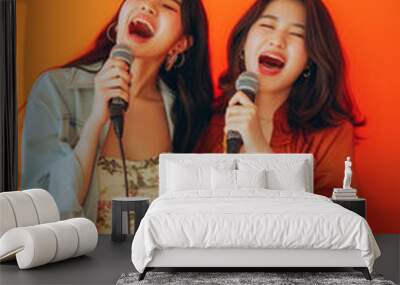 two asian woman with microphones singing on front of orange studio background Wall mural