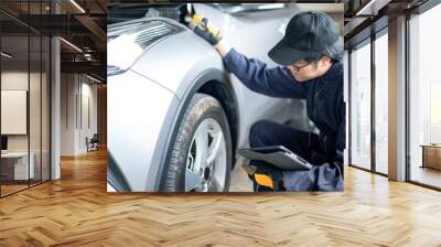 Asian auto mechanic holding digital tablet checking car wheel and tire in auto service garage. Mechanical maintenance engineer working in automotive industry. Automobile servicing and repair concept Wall mural