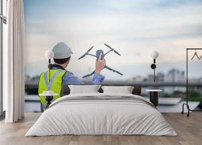 Asian engineer man holding drone at construction site. Male worker using unmanned aerial vehicle (UAV) for land and building site survey in civil engineering project. Wall mural