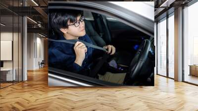 Driving safety concept. Asian businessman fasten seat belt while sitting on driver seat in modern car. Land vehicle for urban lifestyle. Wall mural