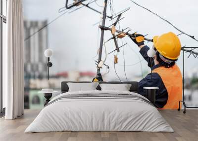 Male electrical worker or Asian man electrician wearing safety helmet and reflective suit repairing an old TV antenna and cable on rooftop of building. Wall mural