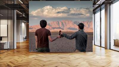 Two Asian man traveler clinking bootle drinking beer while looking at scenery during the sunset in Namibia, Africa. Friendship, travel and celebration concepts Wall mural