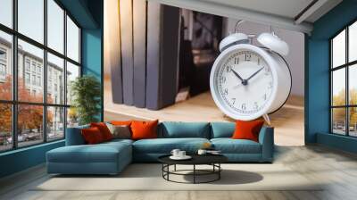 White table clock and books on wooden bookshelf in living room. Home decoration. Time concept Wall mural