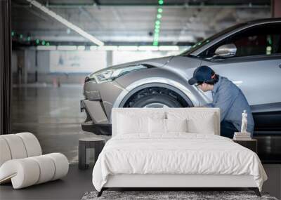 Young Asian auto mechanic holding digital tablet checking car wheel in auto service garage. Mechanical maintenance engineer working in automotive industry. Automobile servicing and repair concept Wall mural