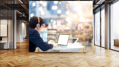 Young Asian business man listening to music by headphones while working with laptop computer in co working space. freelance or digital nomad lifestyle in urban workspace concepts Wall mural