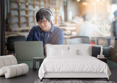 Young Asian man working with his laptop computer and holding coffee cup in library. high school or university college student, educational concepts Wall mural