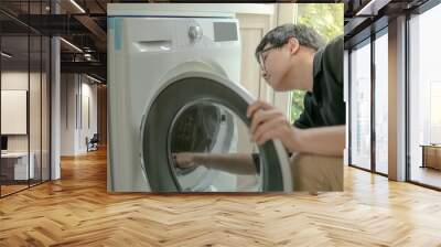 Young Asian technician looking into washing machine checking inside. Appliance maintenance in laundry at home. Technology concept Wall mural