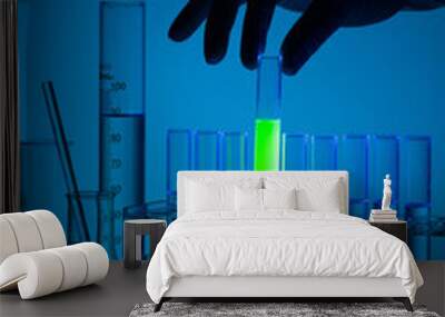 close up of a hand holding chemistry test tube with green fluorescence in lab. Wall mural