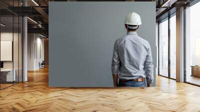 A male engineer stands with his back to the camera, wearing a white hard hat and casual shirt. The neutral gray background and simple attire highlight the professional nature of the construction Wall mural